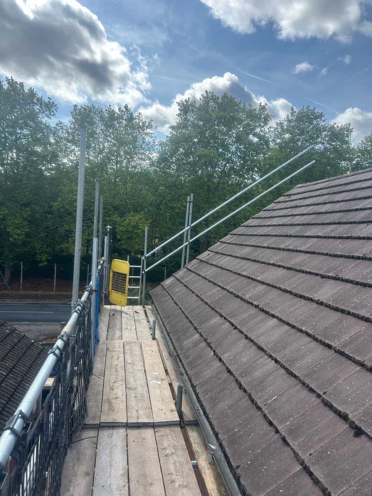 A roof of a house with a scaffolding and trees in the background.